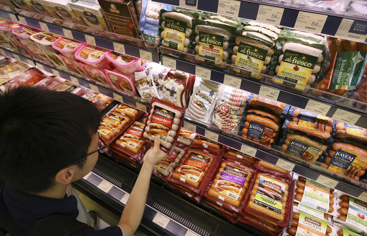 A customer chooses from preserved sausages and hams at a supermarket.