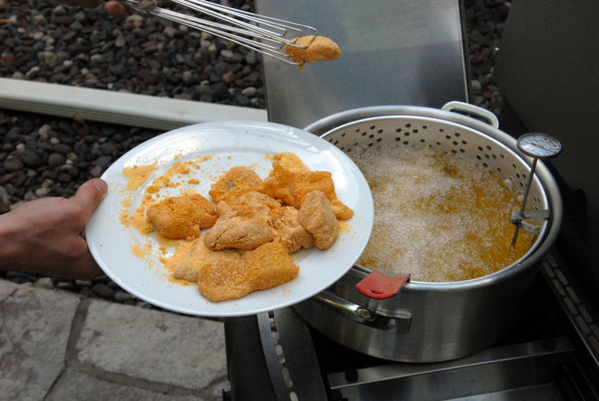 A person removes fried fish fillets from a frying pan.