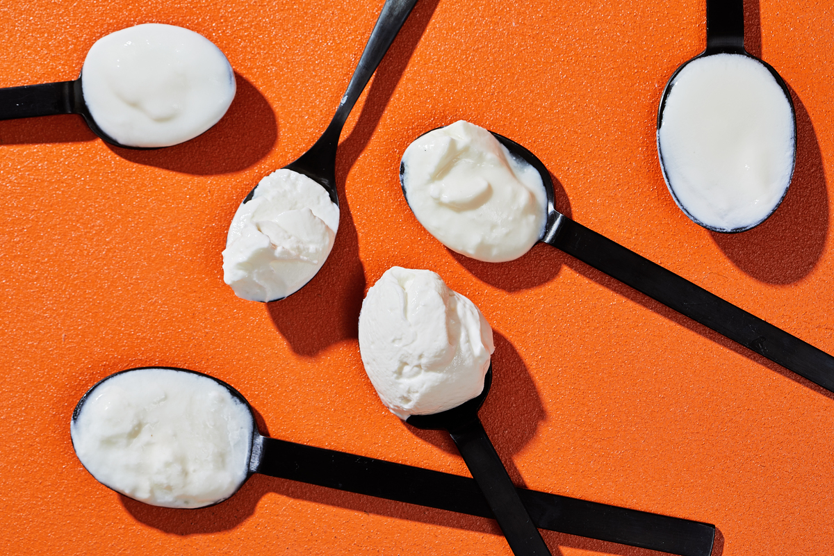 Spoonfuls of yogurt lie against an orange table.