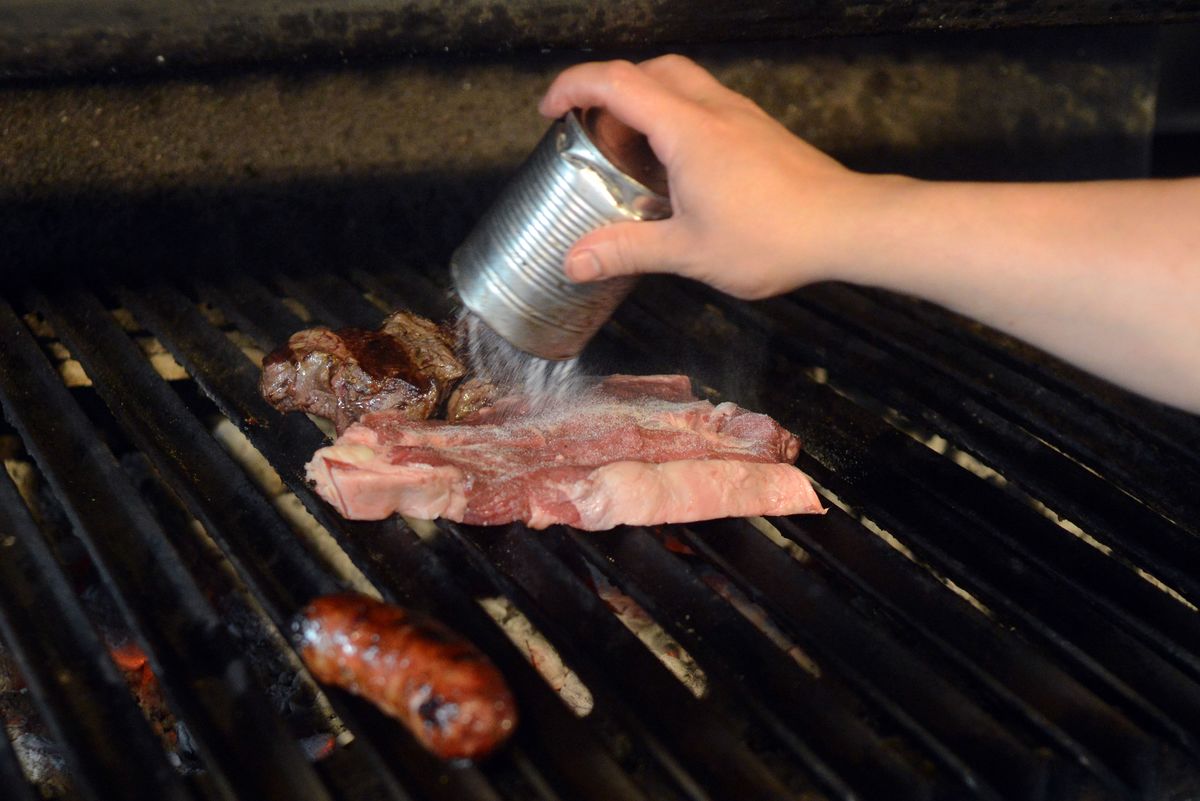 A cooker puts salt on beef in a traditional grill restaurant.