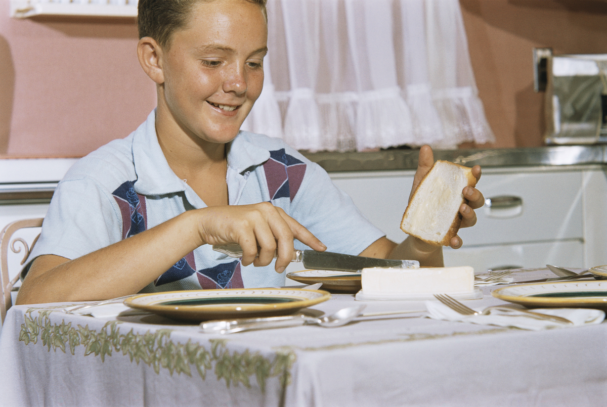 A boy spreads butter on white bread.