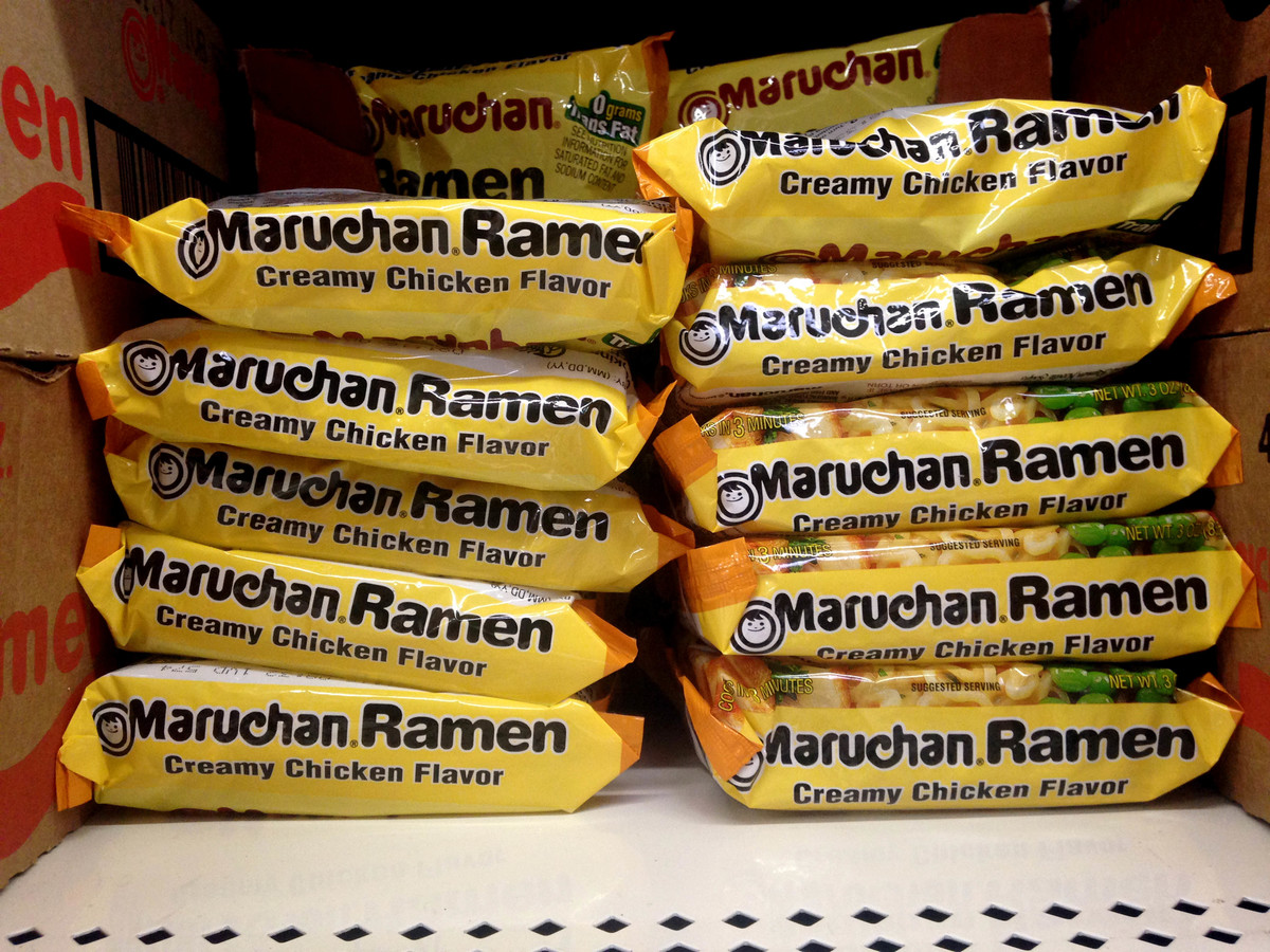 Dried ramen noodle packages are stacked on a store shelf.