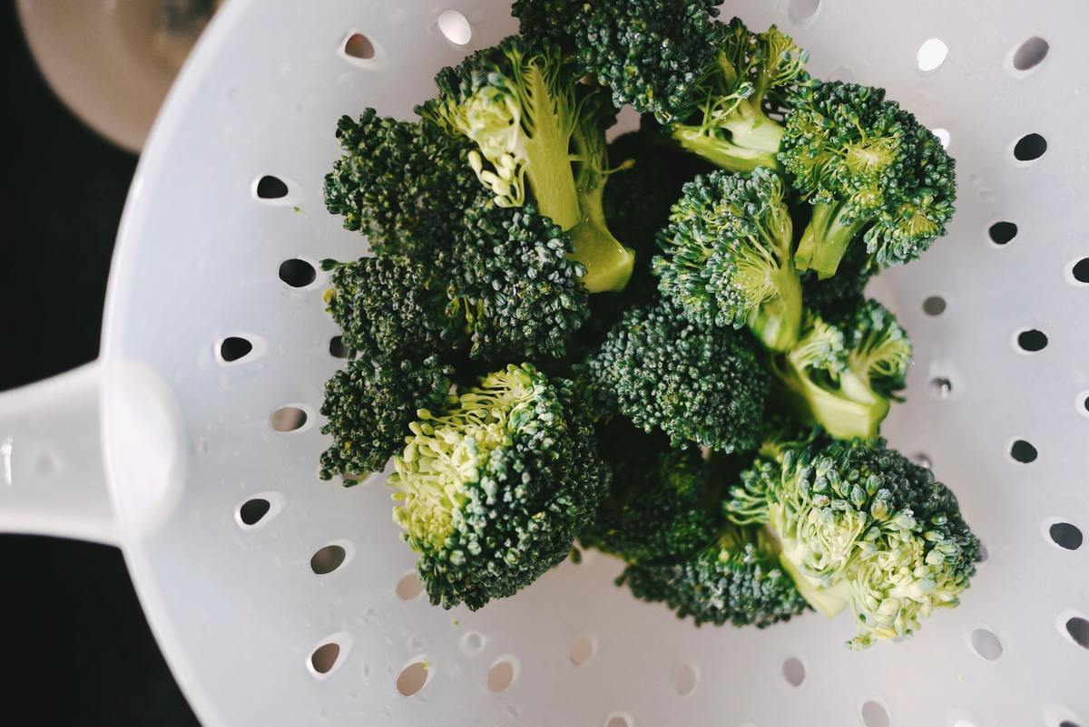 Person cleans broccoli with a strainer.