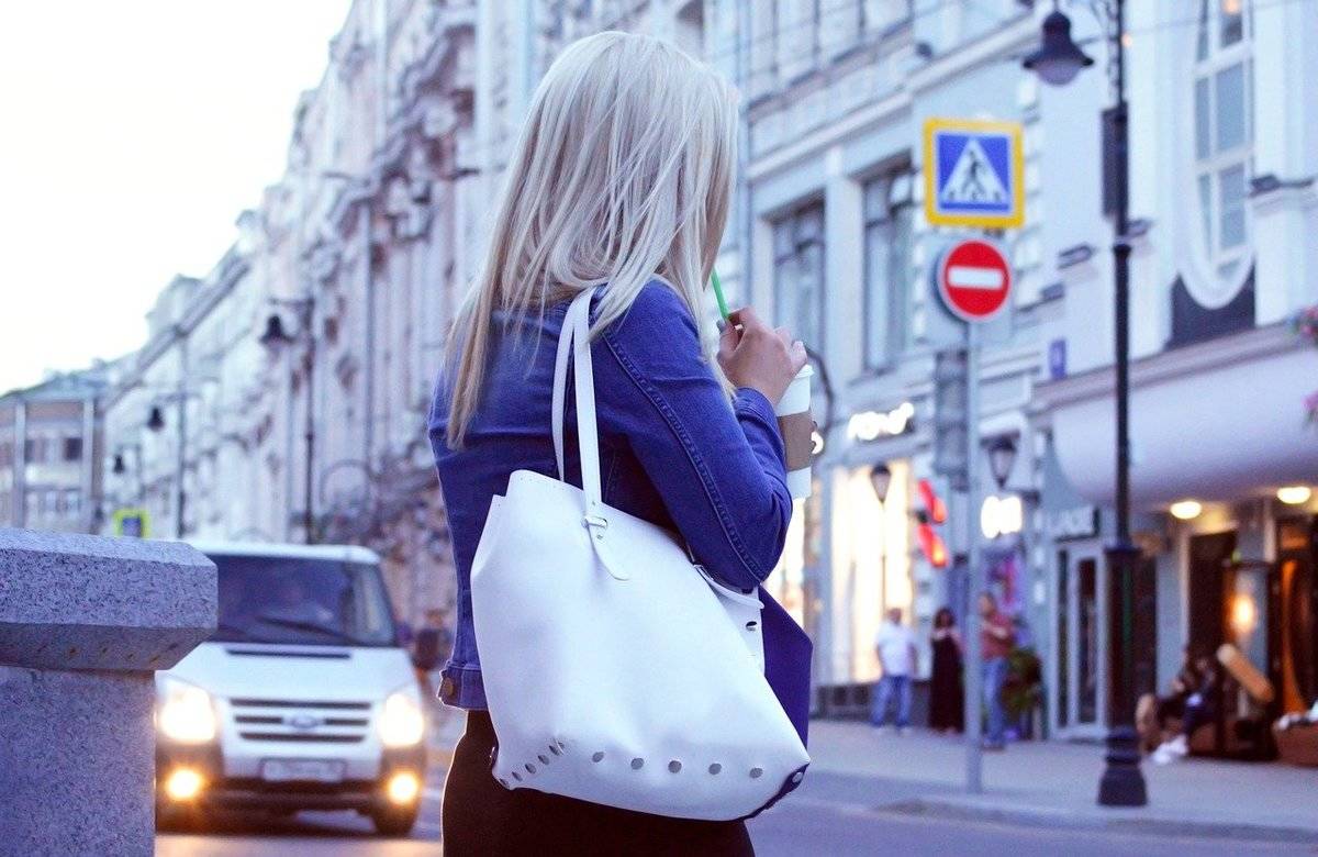 A woman carries a purse while she crosses the street.