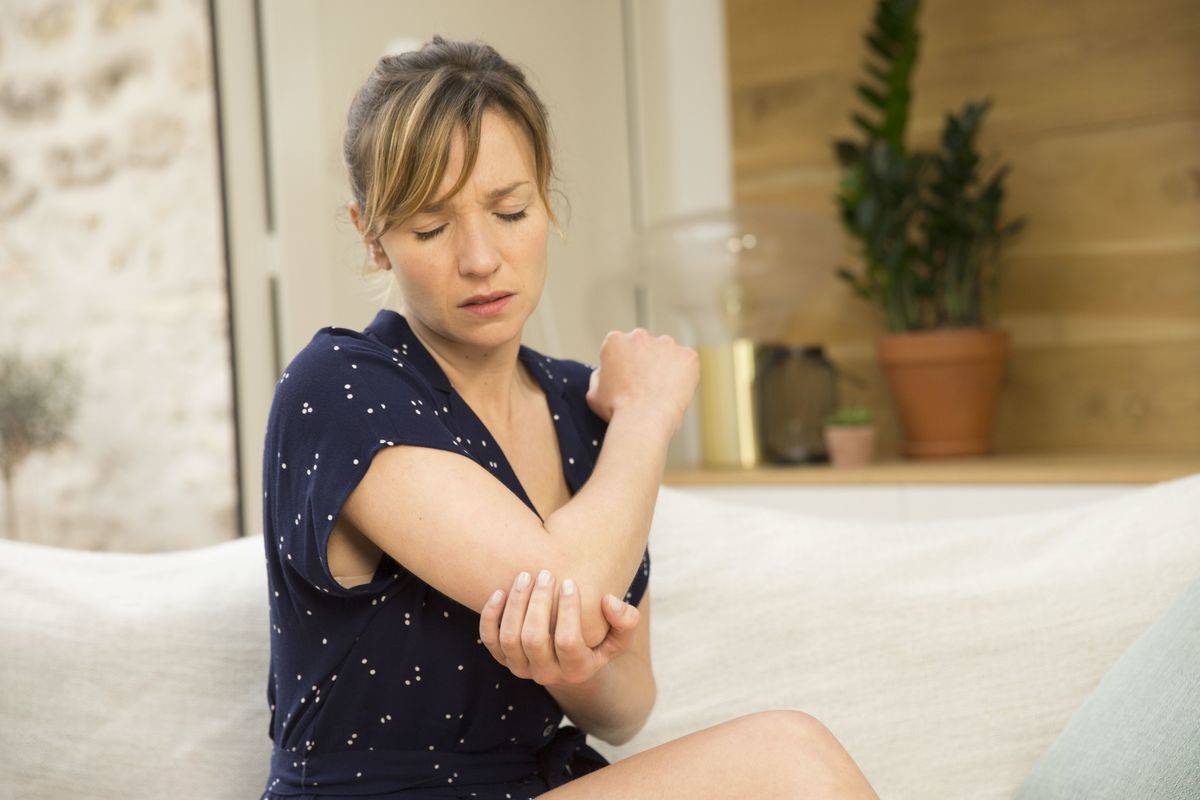 A woman clutches her elbow in pain.