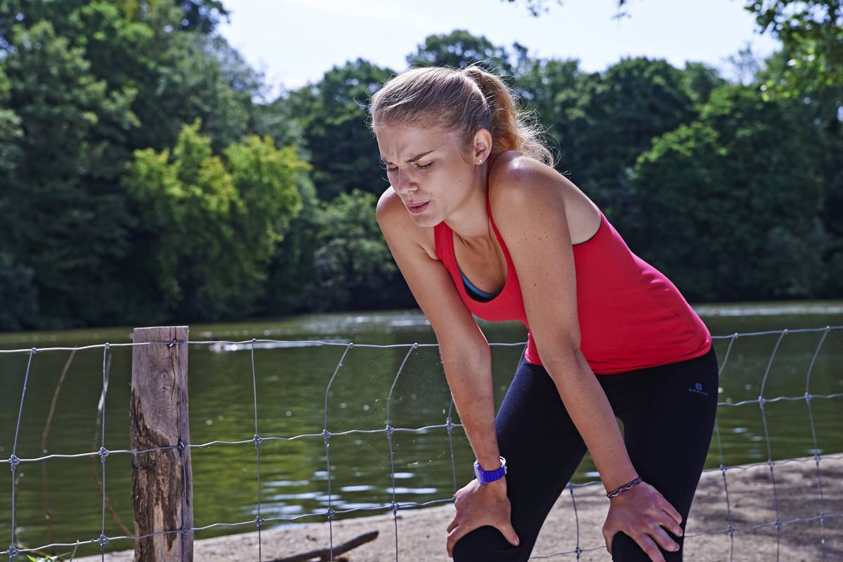 After running, a woman places her hands on her knees and rests.