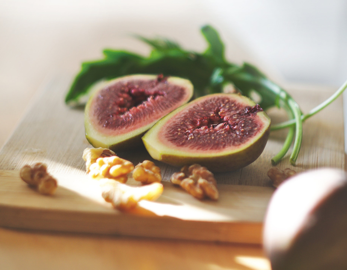A cut fig lies on a cutting board with arugula and walnuts.