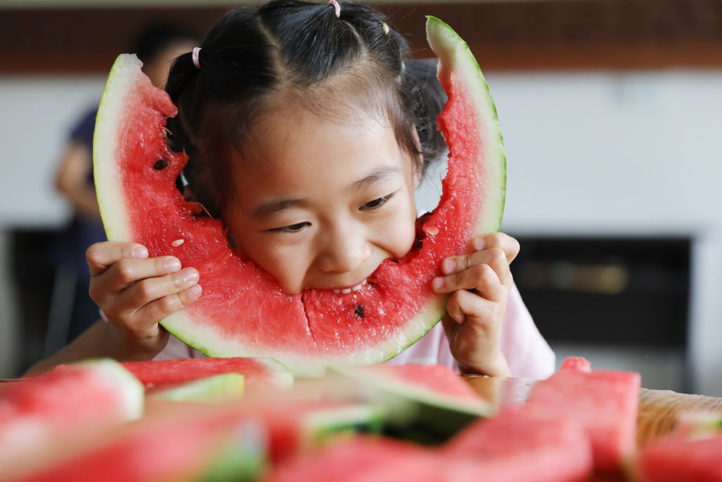 a young girl eating a big piece of watermelon