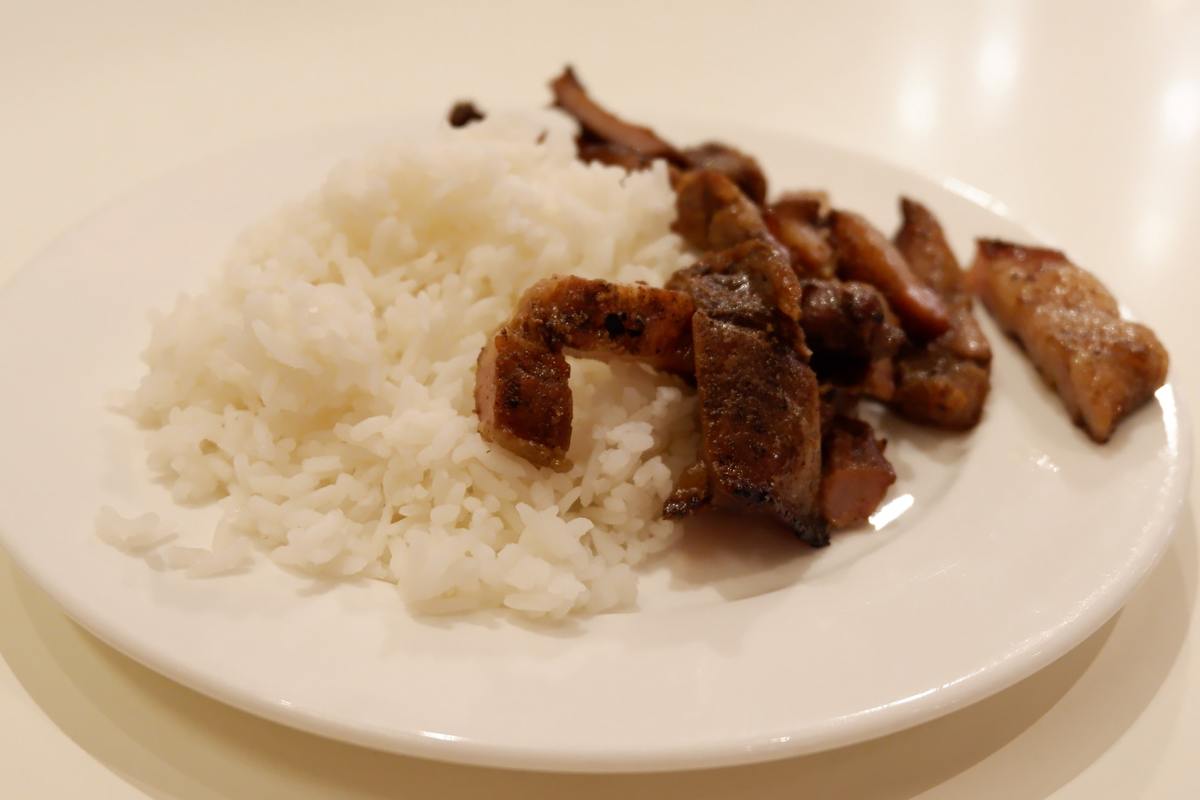 A plate holds white rice and pork.