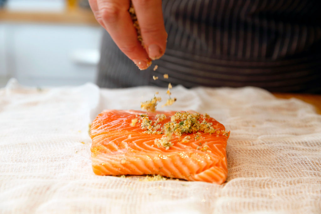 someone sprinkling a citrus rub on a salmon filet