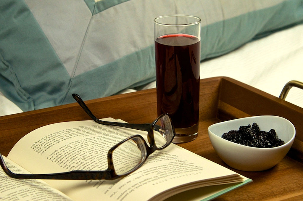 tart cherry juice, a book, glasses, and dried fruit on a bedside tray